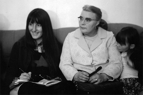 Production still from Nightcleaners: Image shows 2 women and a small girl sat on a sofa. One of the women is writing on some paper